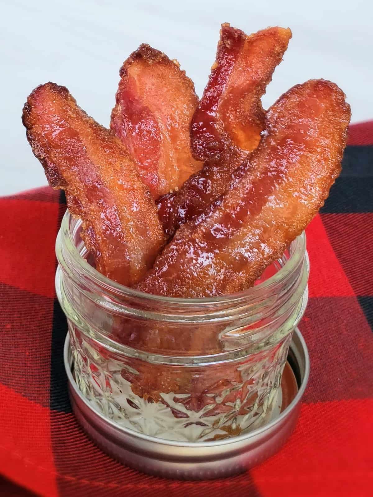 Stacked candied bacon in 4 ounce canning jar on red and black checked fabric