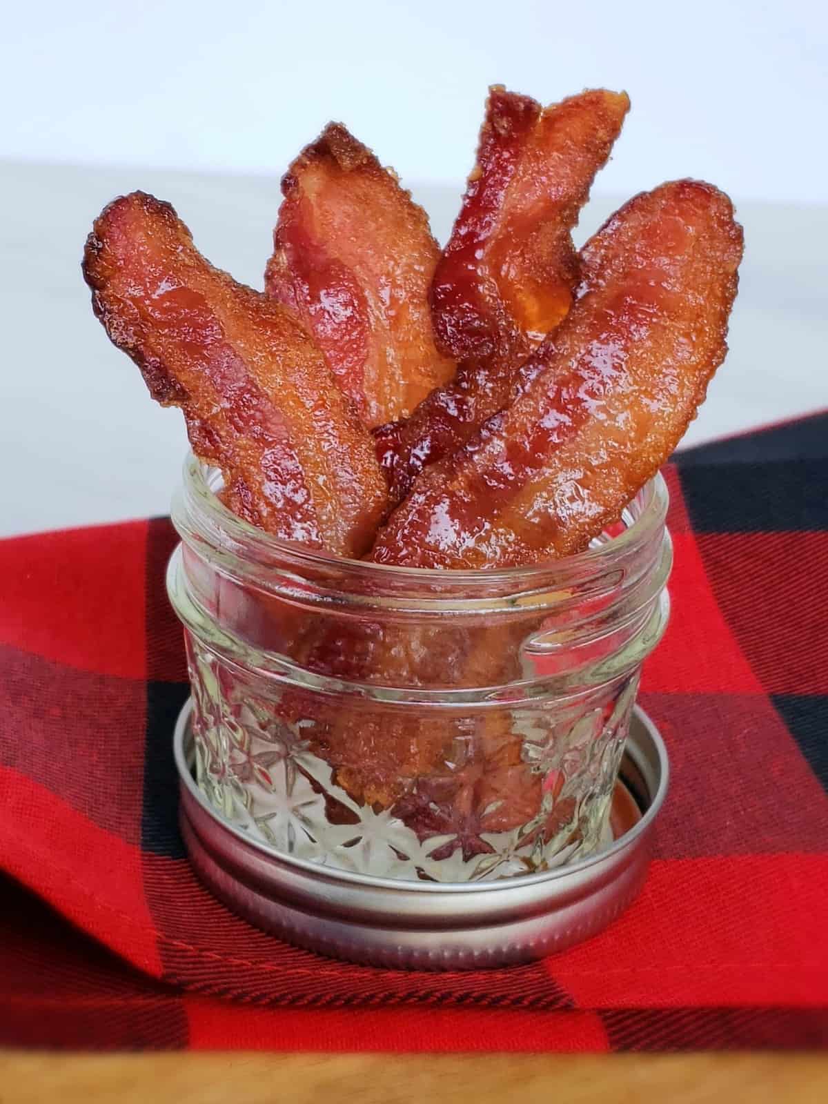 Stacked candied bacon in 4 ounce canning jar on red and black checked fabric