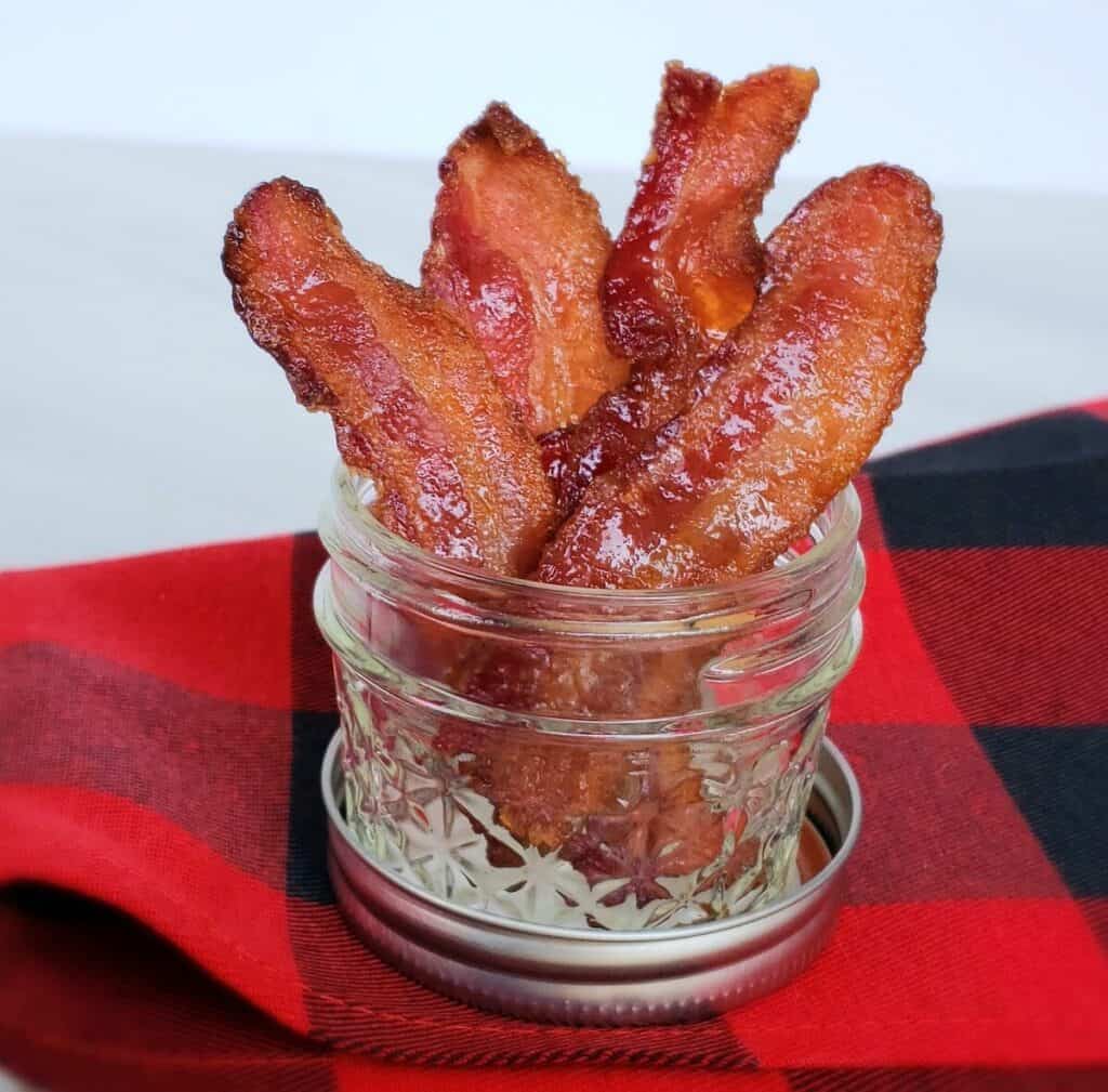 Stacked candied bacon in 4 ounce canning jar on red and black checked fabric