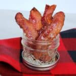 Stacked candied bacon in 4 ounce canning jar on red and black checked fabric