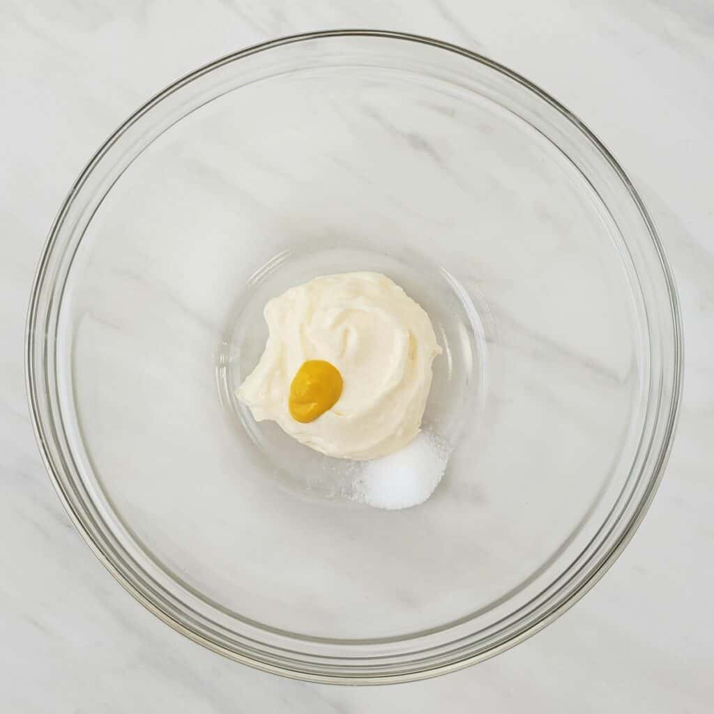 Mayonnaise, mustard, and salt in a clear glass bowl on a marble surface