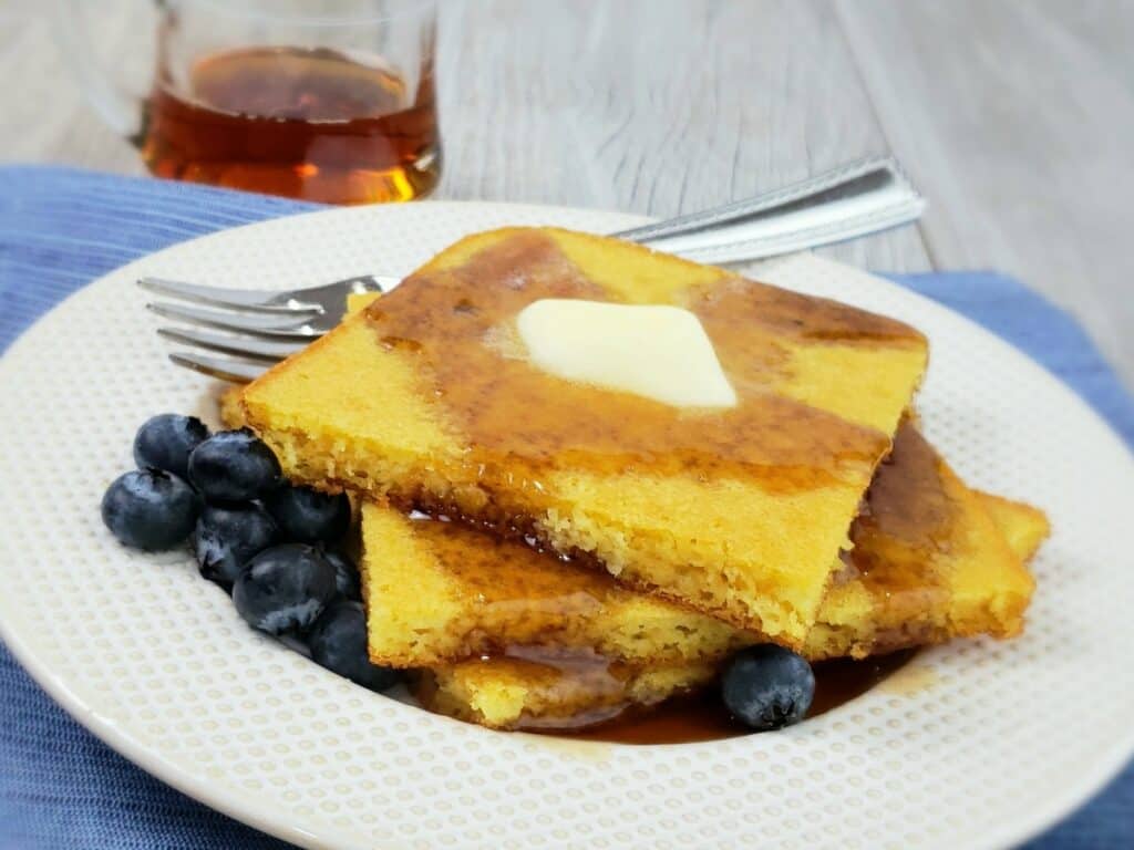 Stack of square pancakes with butter and blueberries on white plate