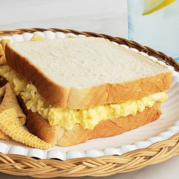Egg salad sandwich on a paper plate and wicker charger