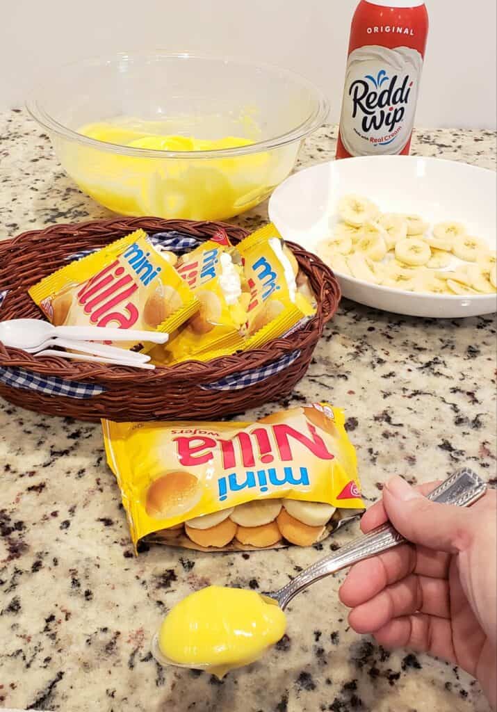 bags of mini vanilla wafers in a brown basket with sliced bananas and a bowl of pudding