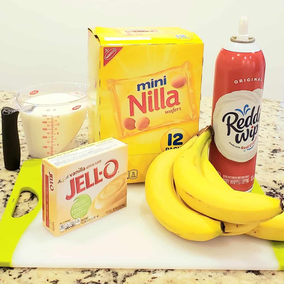 Ingredients for Walking Banana Pudding on a white cutting board: bananas, Redi whip, Nilla wafers Jello pudding milk