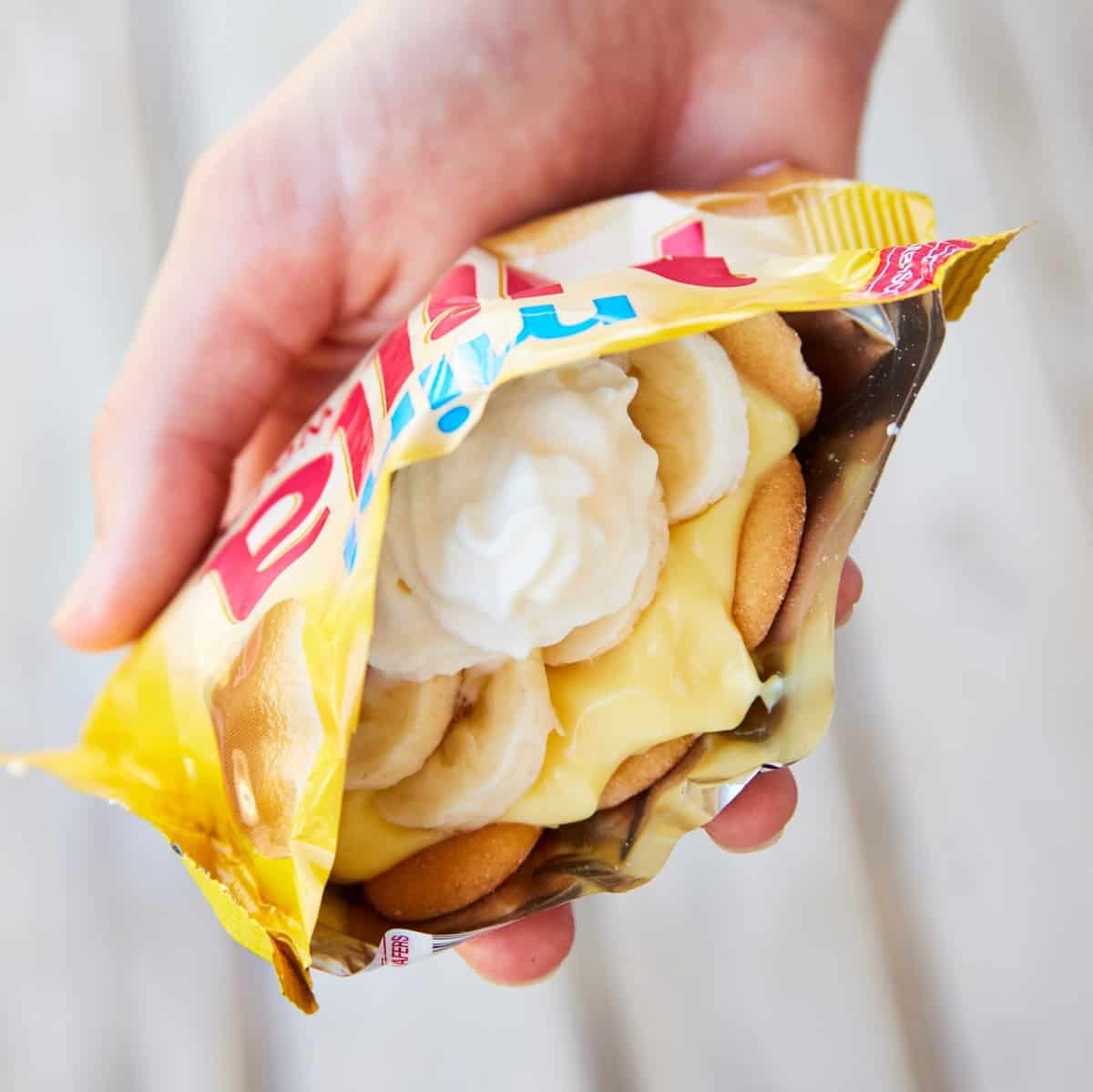 A hand holding a vanilla wafer bag filled with banana pudding.