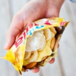 A hand holding a small bag of vanilla cookies with bananas and whipped cream on them.
