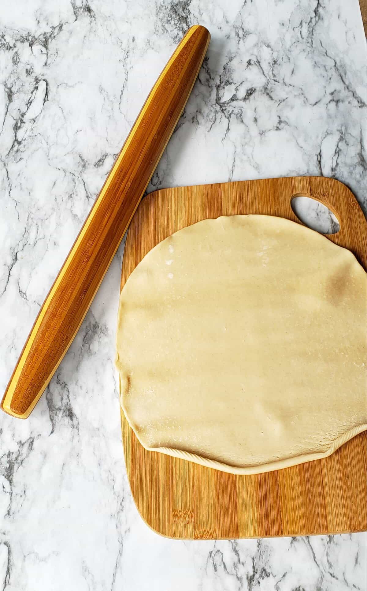 Circle of pie dough on wooden cutting board with wooden rolling pin