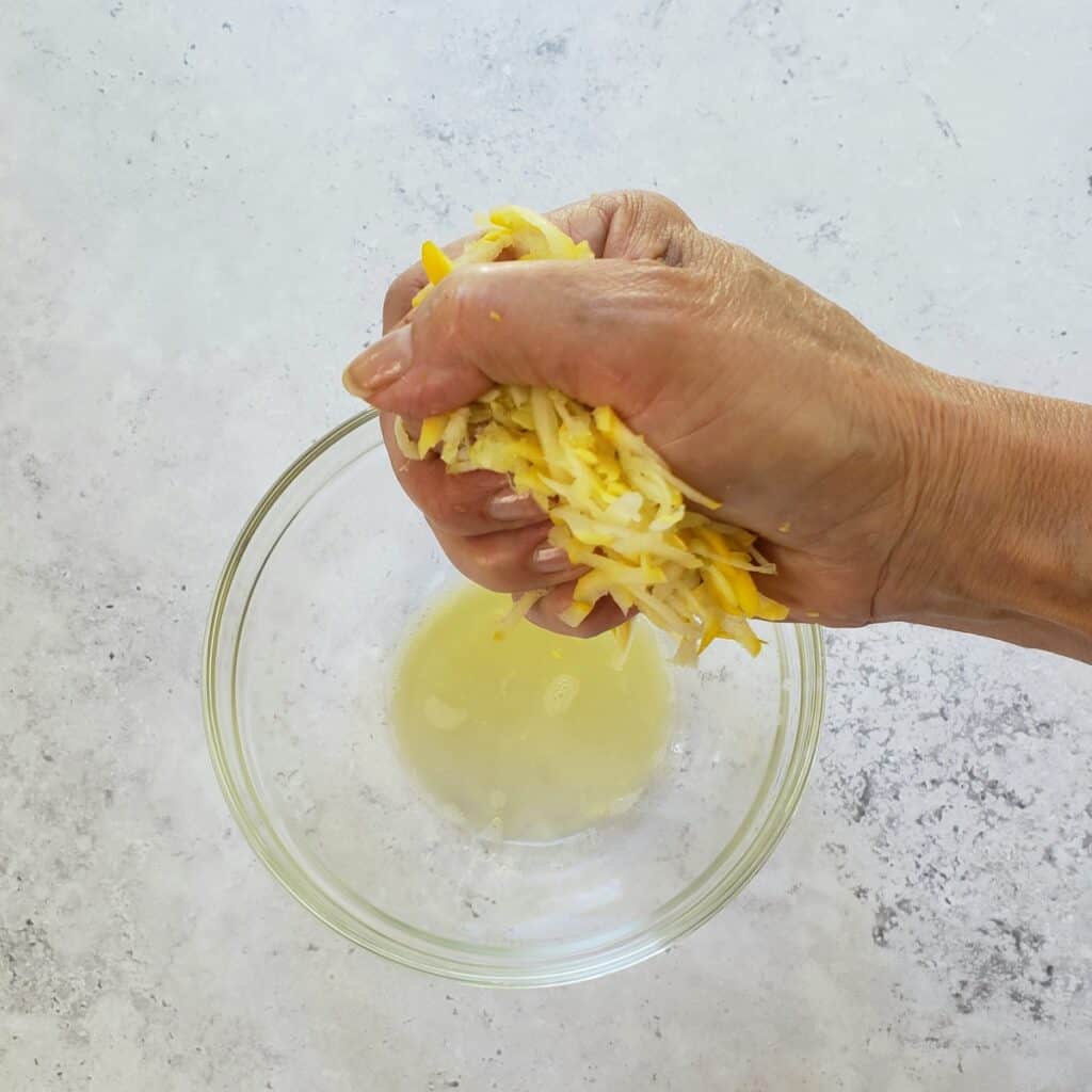 a hand squeezing shredded yellow squash into a bowl