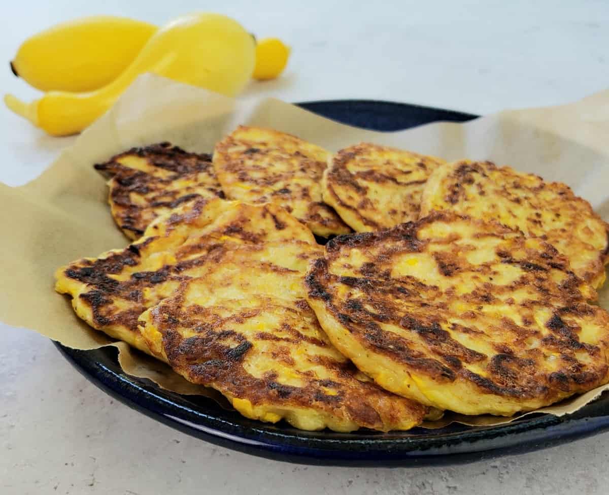 a blue plate of yellow squash fritters with 2 squash in background