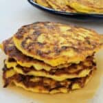 stack of yellow squash fritters with blue plate of fritters in background