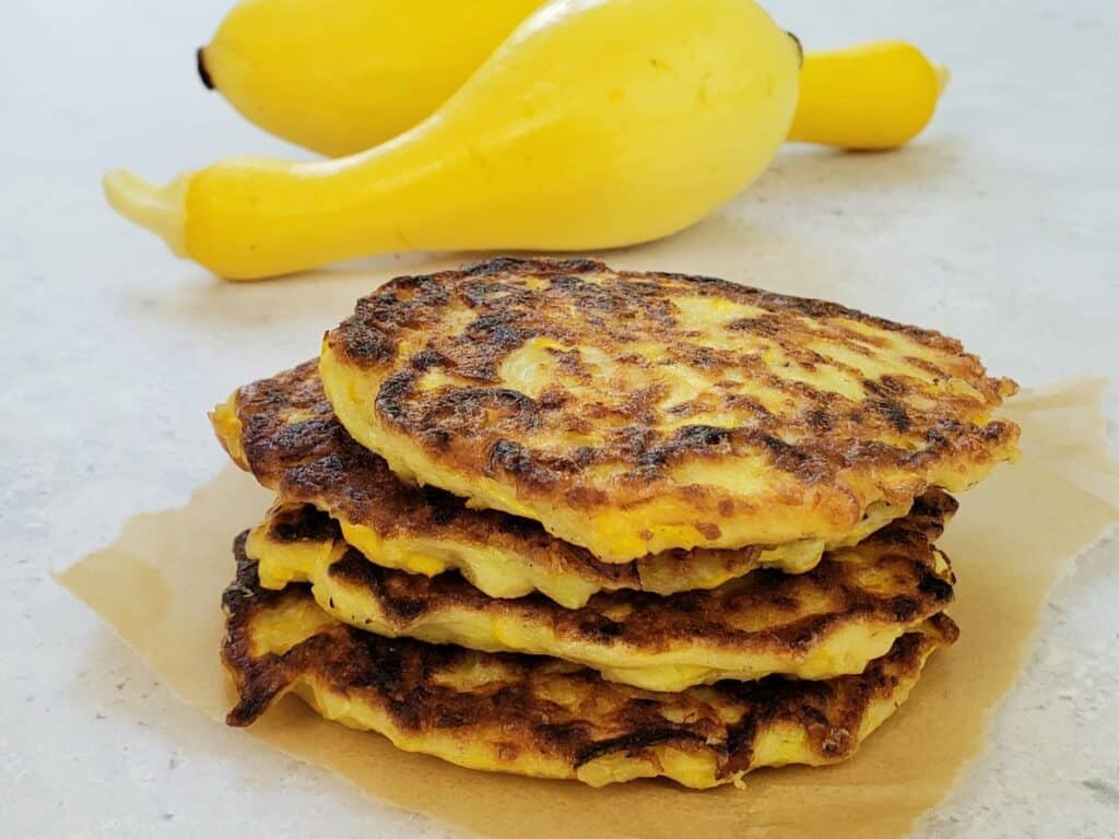 a stack of 4 squash patties with 2 yellow squash in background