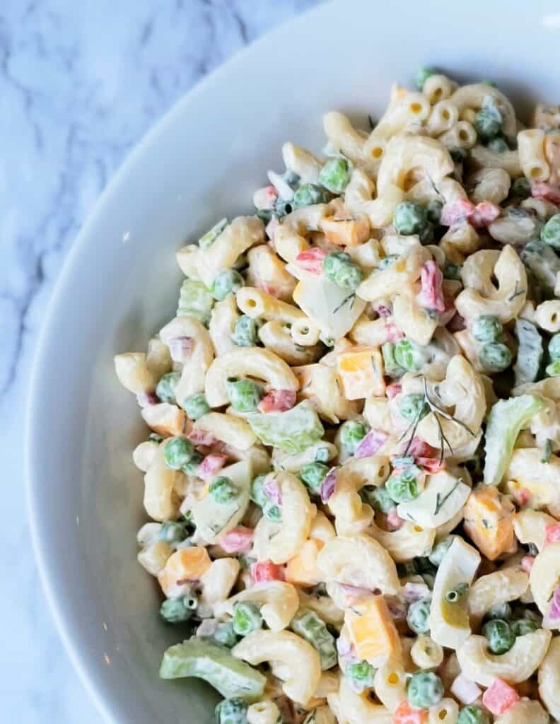 Close up edge of white bowl of macaroni salad on marble surface