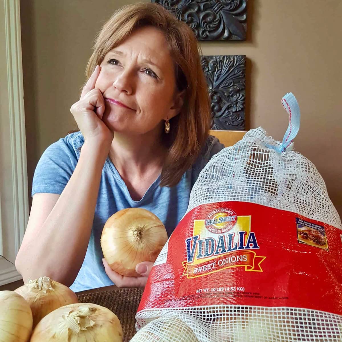 Woman holding a Vidalia onion sitting next to a large bag of onions.