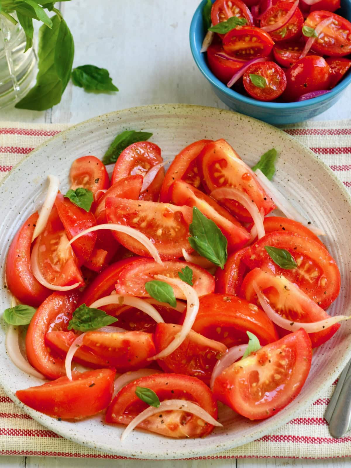 Tomato and onion salad in a large bowl with basil leaves.