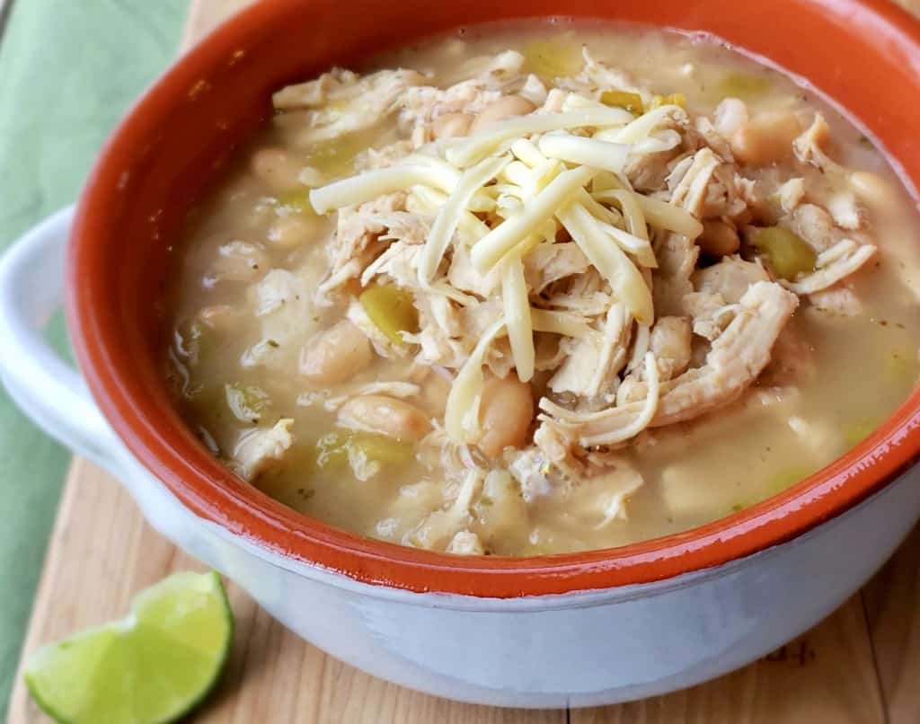 Ceramic bowl of white bean chicken chili with lime wedge on wooden cutting board