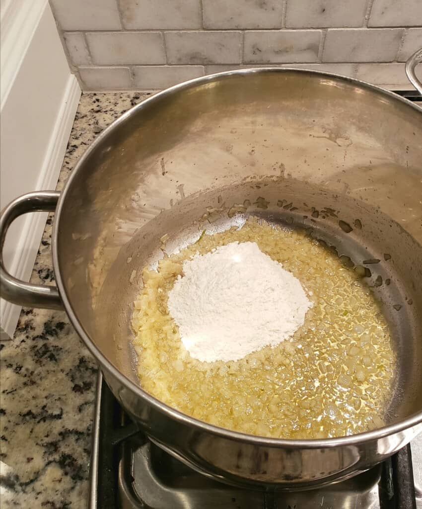 Large pot with melted butter, onion, and a scoop of flour on the stove top.