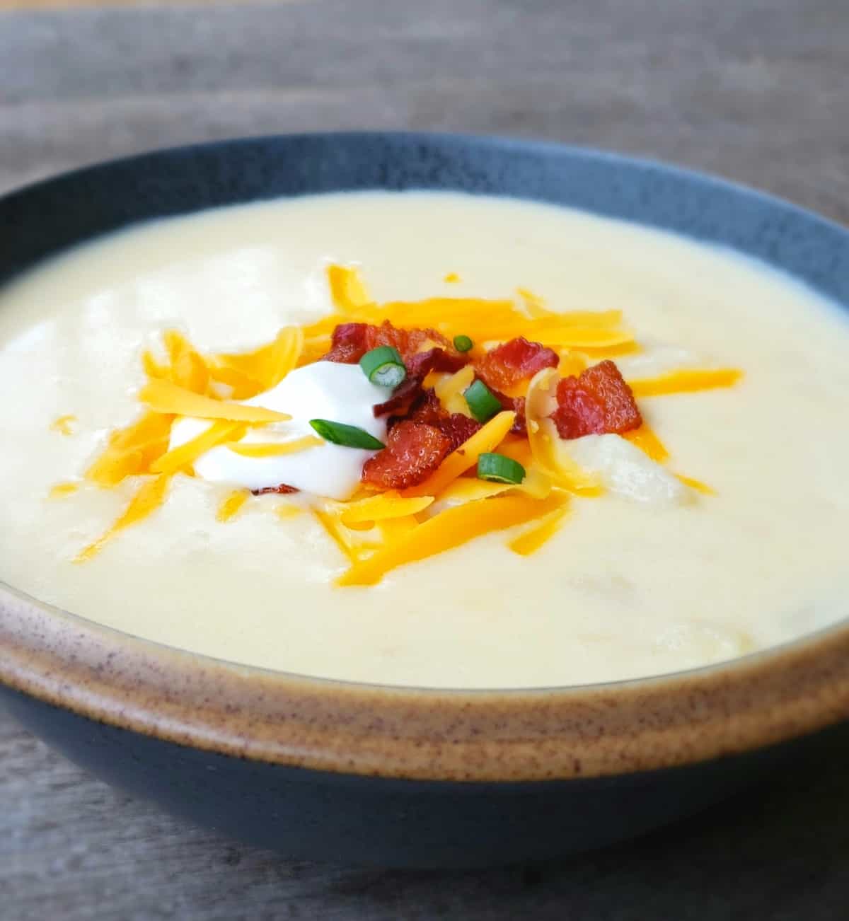 Close up view bowl of potato soup topped with cheese, bacon, sour cream and green oninon.