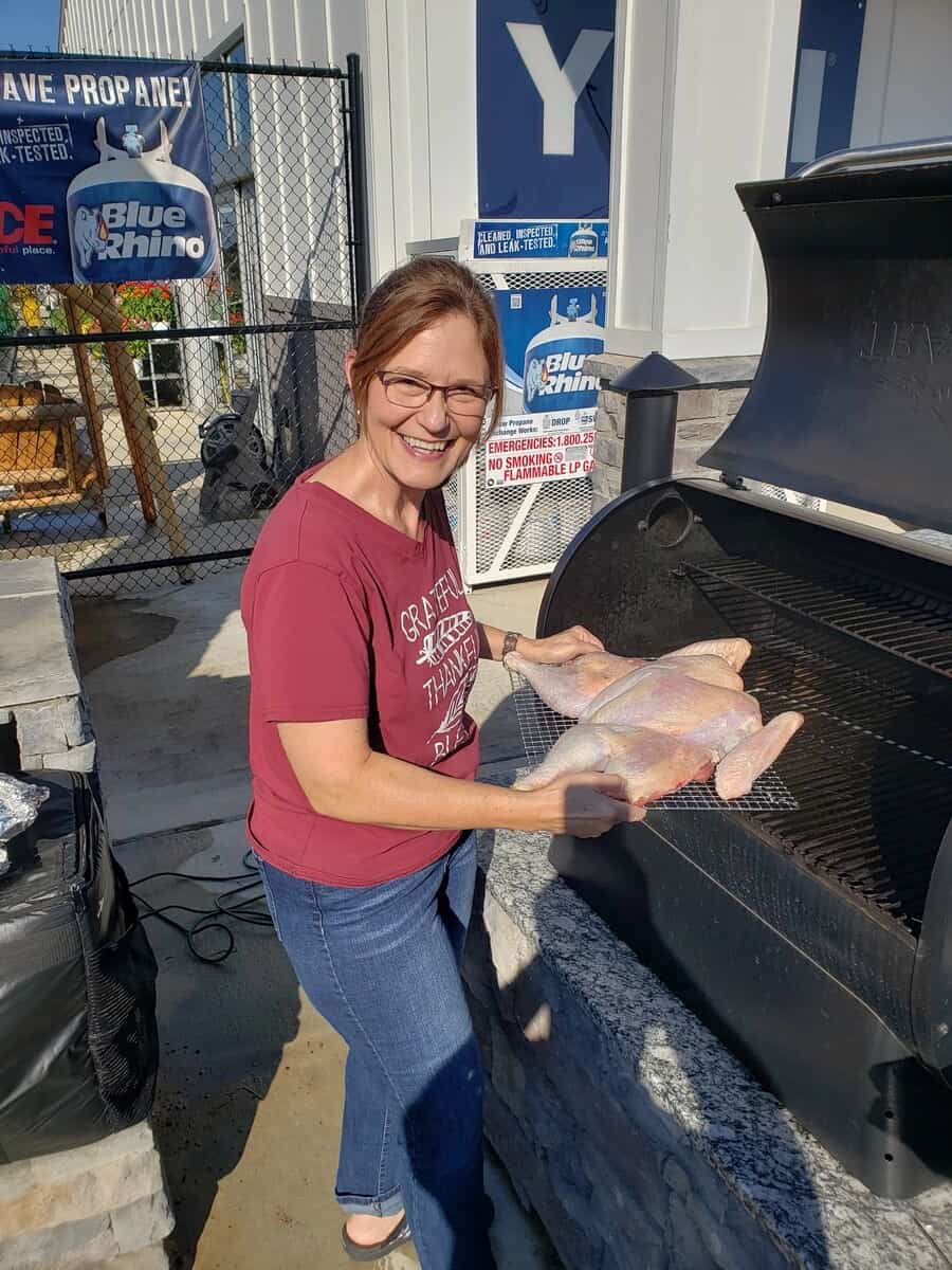 Woman placing flattened turkey on an open grill.
