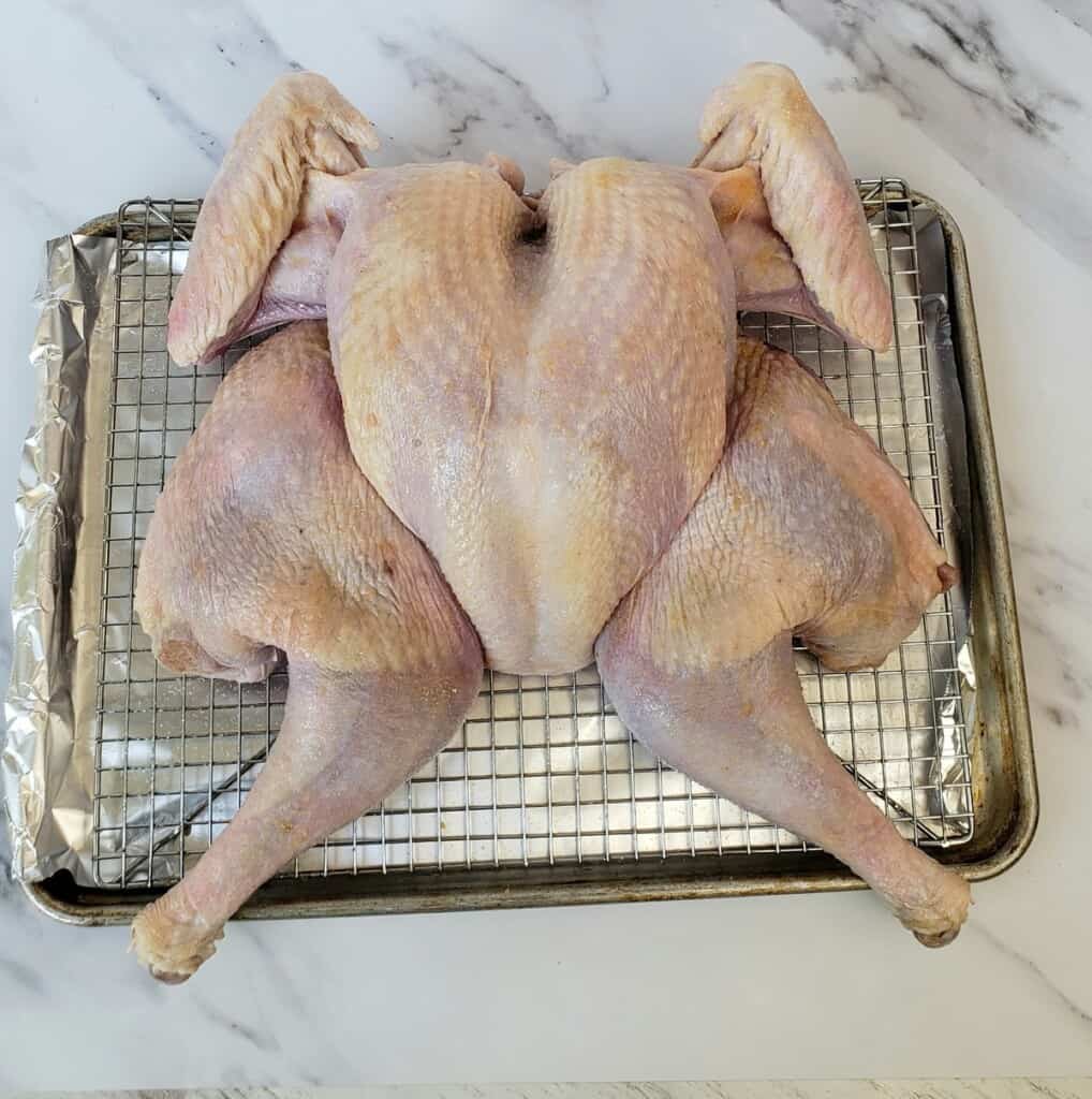 Whole turkey flattened on a rack in a baking sheet