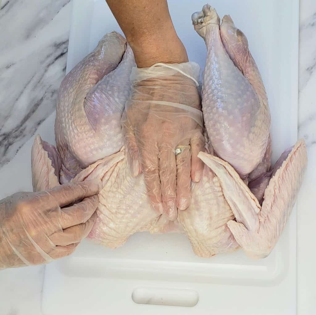 Process shot of a hand pressing down on a raw turkey.