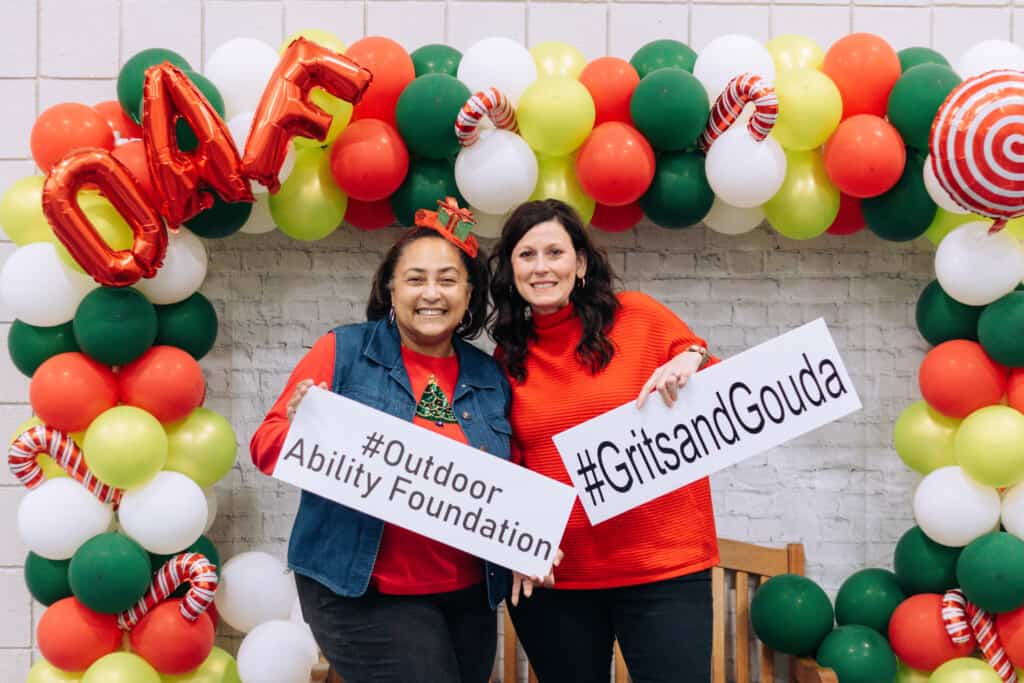 Two ladies holding hashtag signs in front of Christmas balloon station