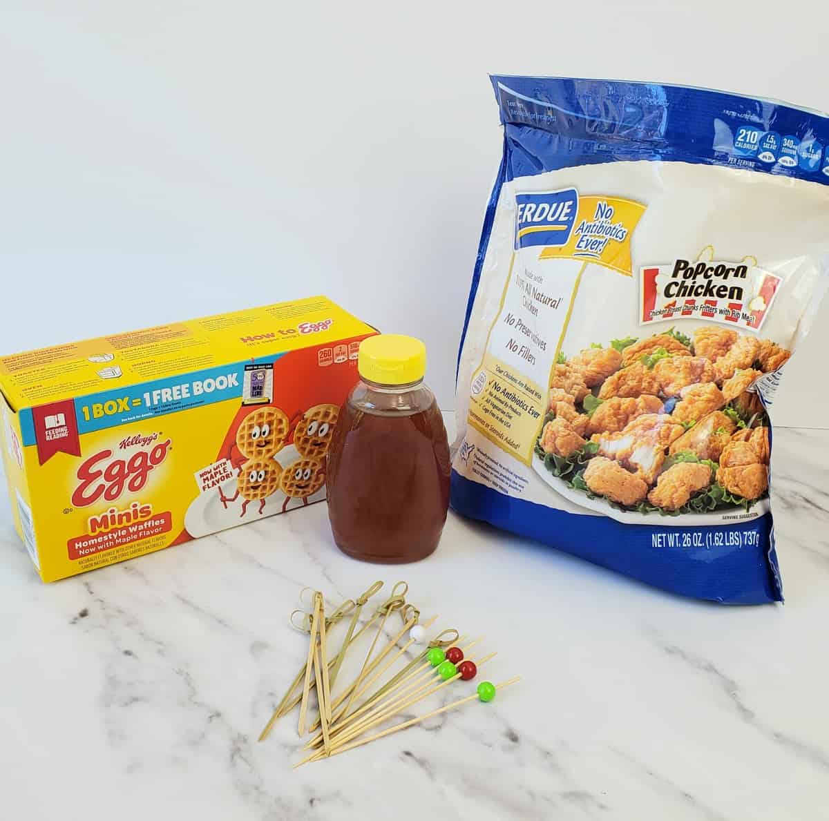 Ingredients on marble surface: Eggo waffle box, honey jar, bag of frozen chicken nuggets.