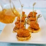 Honey being poured from a clear tiny pitcher onto chicken nuggets and mini waffles.