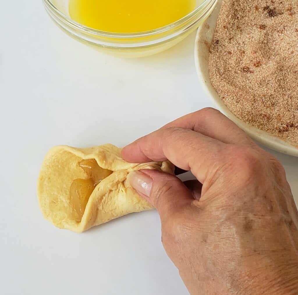 Pinching together biscuit dough filled with apples.