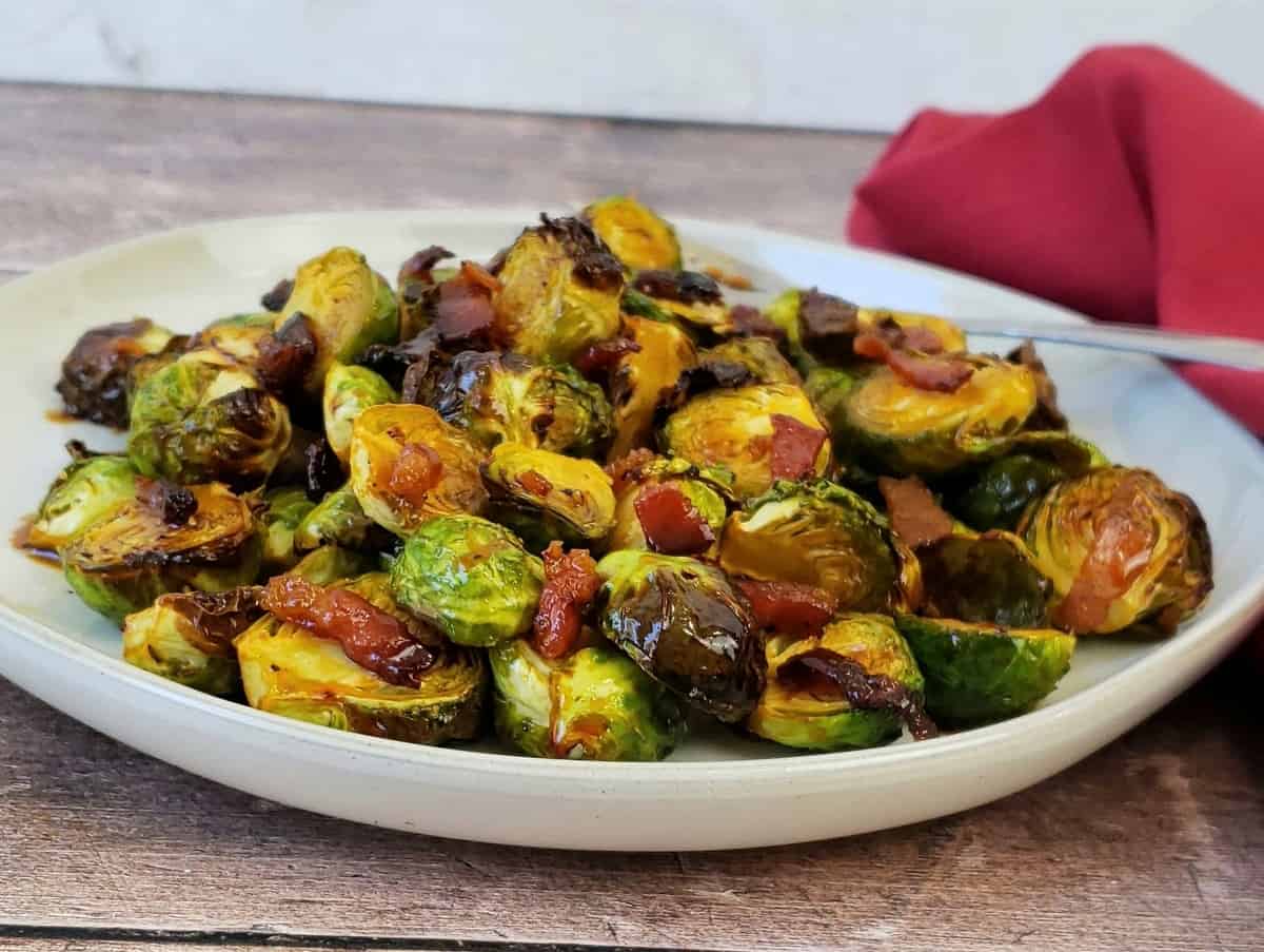 Roasted Brussels sprouts piled up on white plate with red cloth in background.