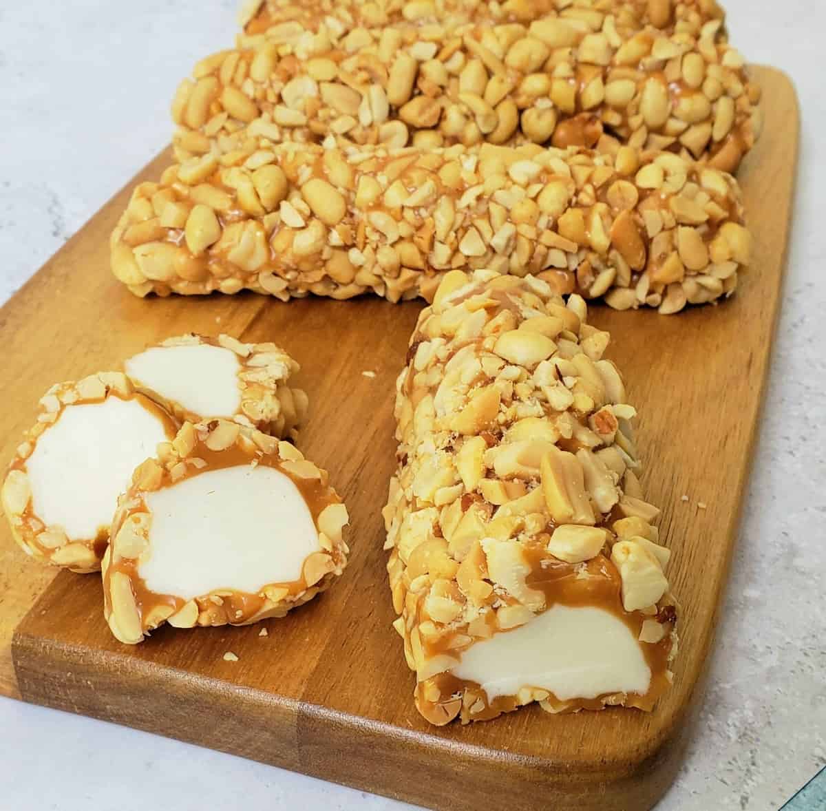 Peanut and caramel covered nougat logs on a wooden board.