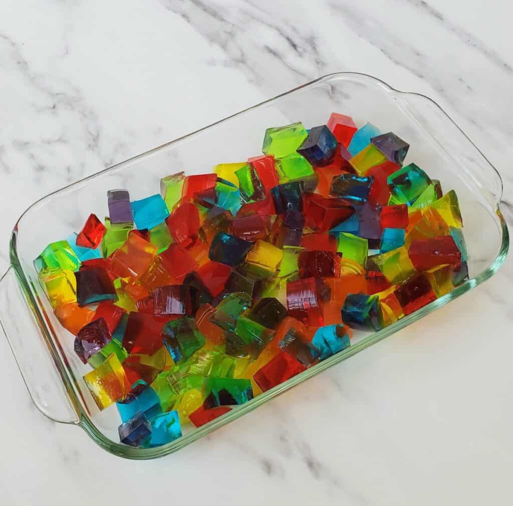 Multi colored cubes of gelatin in a glass rectangle dish.