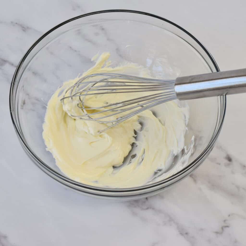 Cream cheese in a glass bowl with a wire whisk.