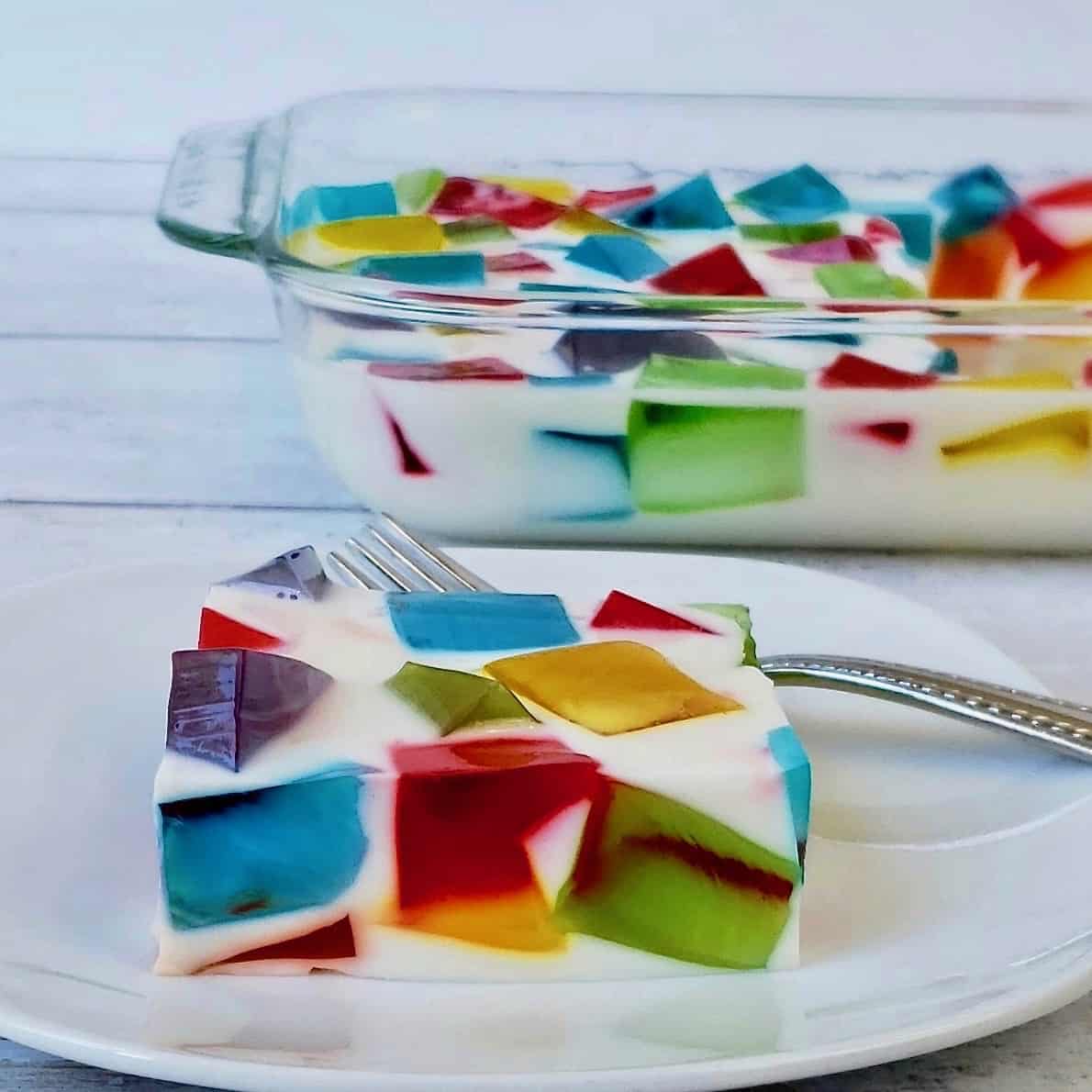 Jello cubes in creamy gelatin salad on white plate; glass casserole dish in background.