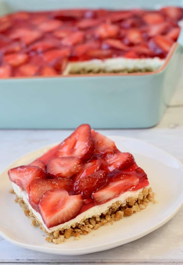 Square slice of strawberry pretzel salad in front of blue 8x8 pan.