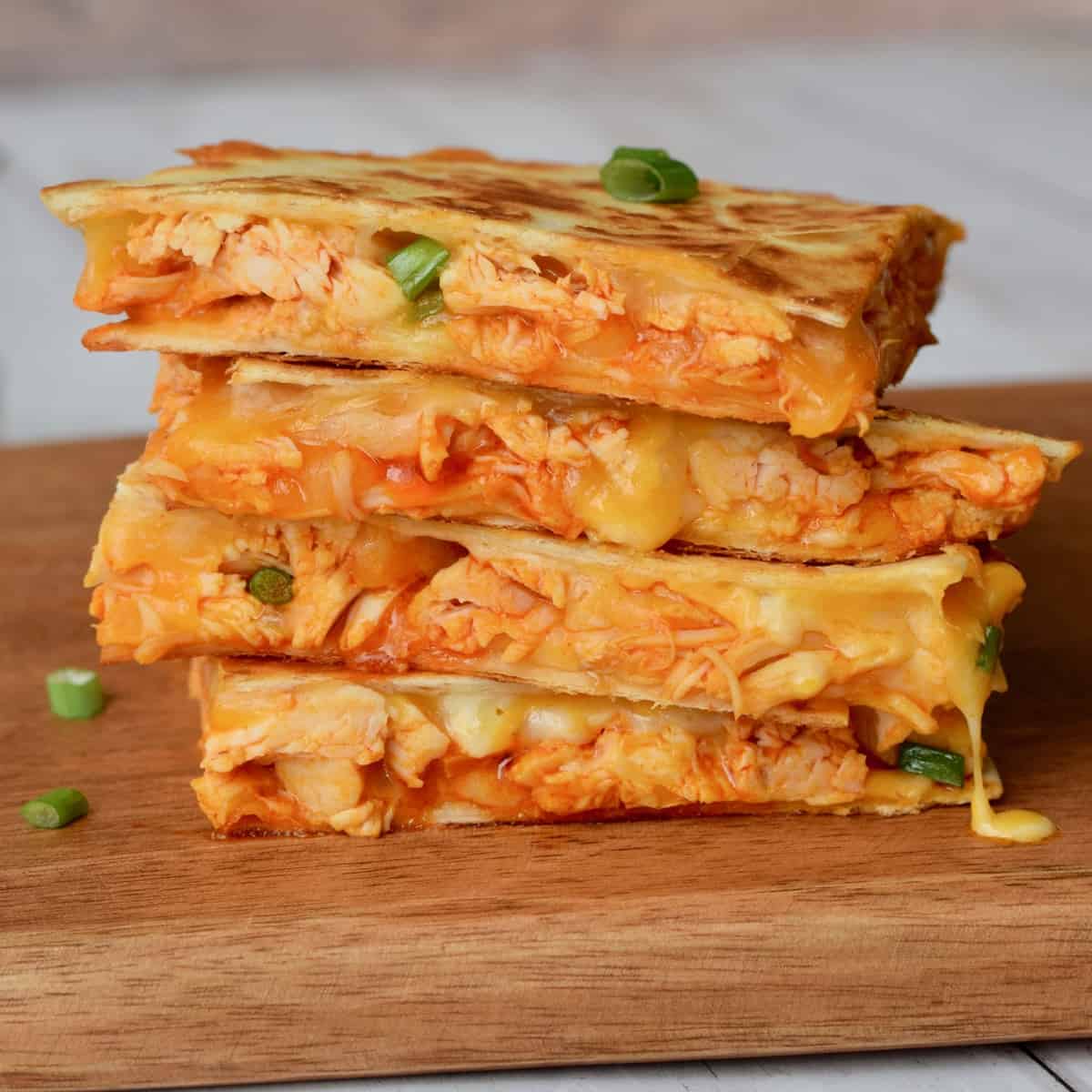 Chicken quesadilla triangles stacked on wooden surface.