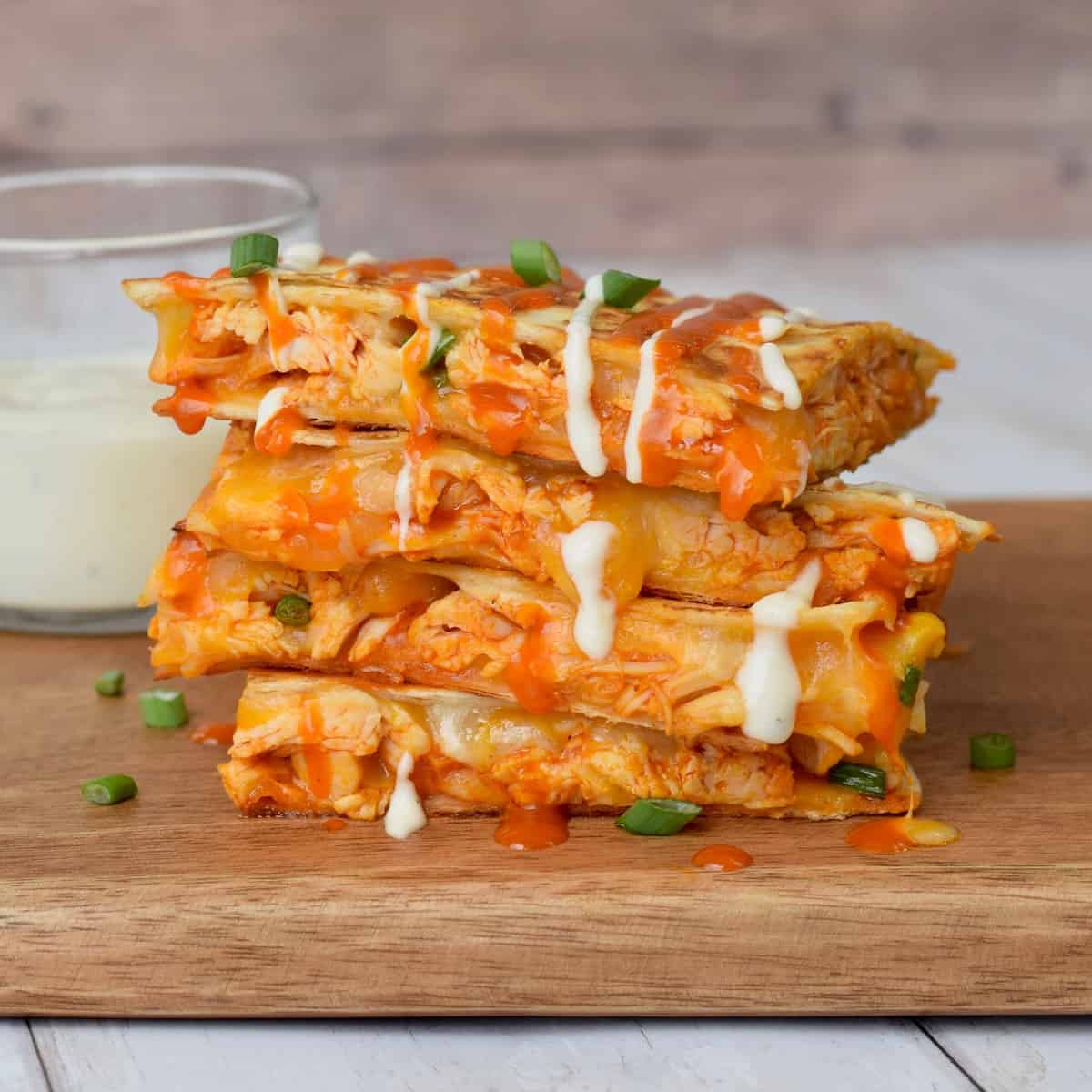 Stack of four triangles Buffalo Chicken Quesadillas on wooden cutting board.