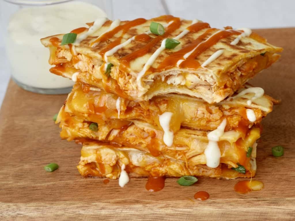 Stack of chicken quesadillas with bite out and sauce dripping.