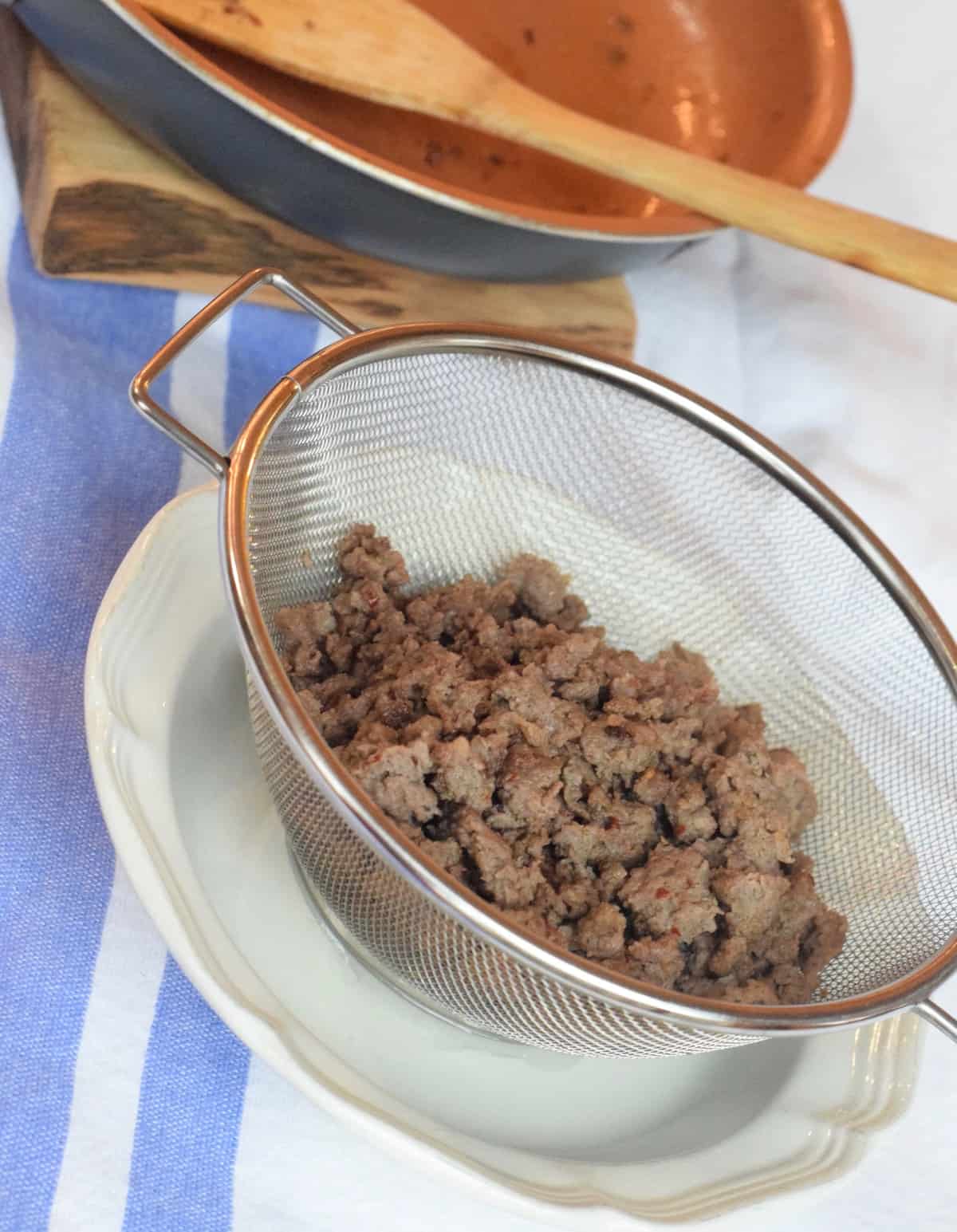 Cooked ground sausage in metal strainer.
