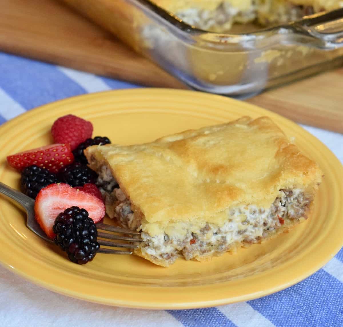 Sausage cream cheese casserole square with fork and fruit on yellow plate.
