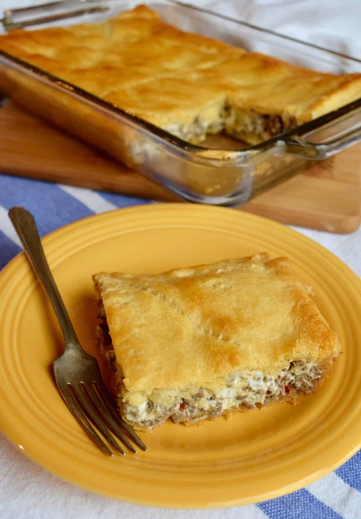 Slice of creamy sausage casserole with a crust on plate with a fork.