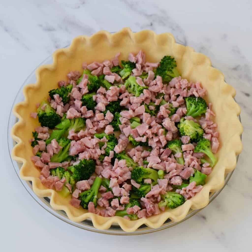 Ham and broccoli in bottom of unbaked pie shell.