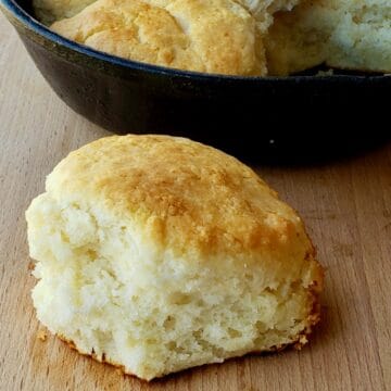 Close up of 2 ingredient biscuit on wooden surface with cast iron skillet in background.