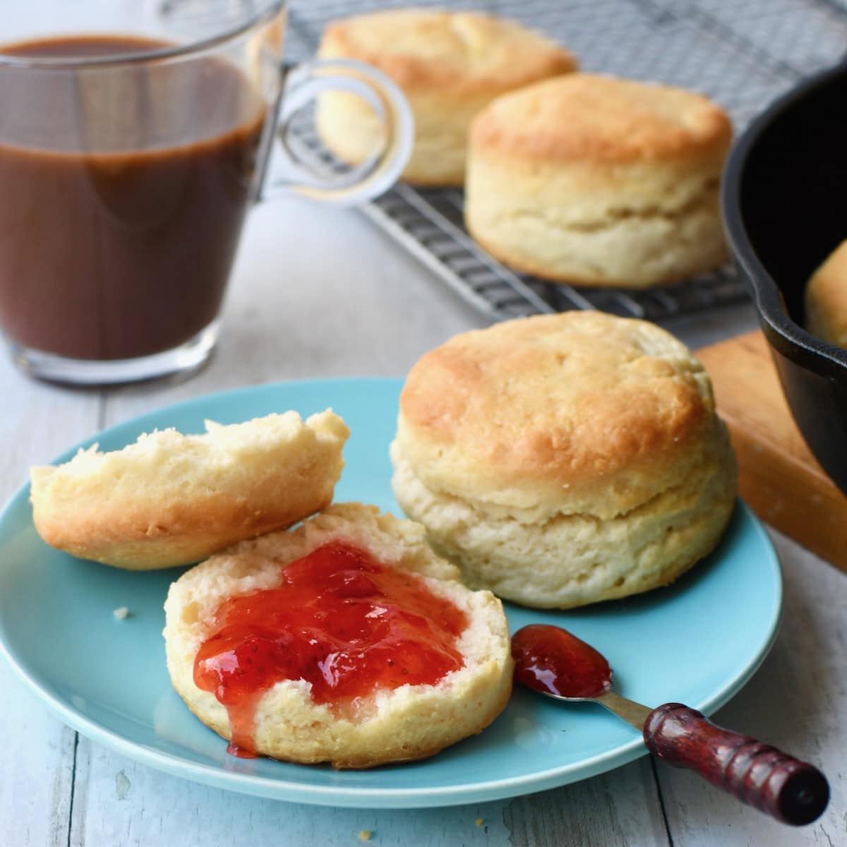 Strawberry jam on open homemade 2 ingredient biscuit on blue plate.