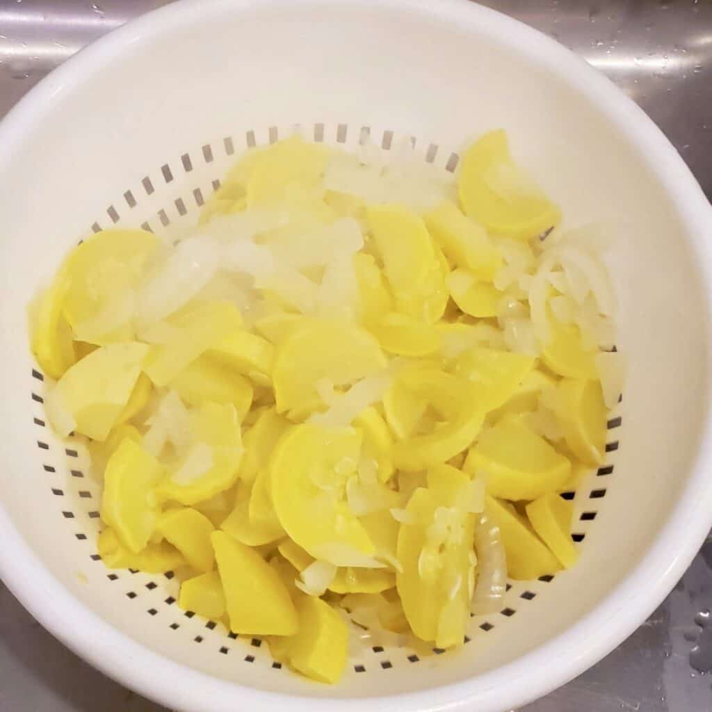 Steamed yellow squash and onion draining in a collandar.