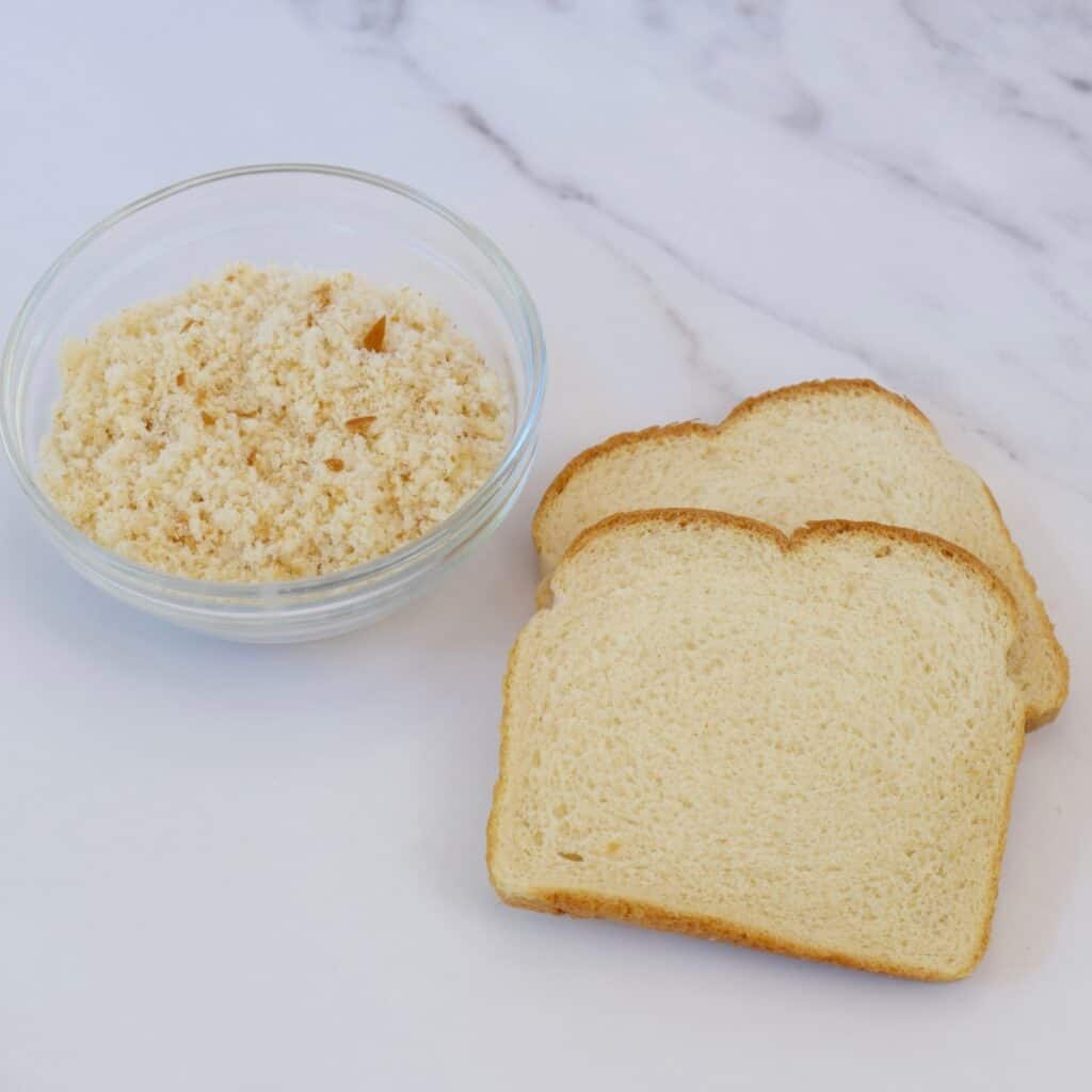 Two slices of bread next to a little bowl of breadcrumbs.