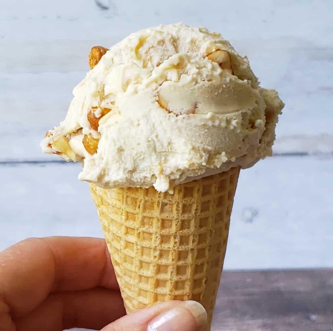 Fingers holding close up scoop of peanut butter ice cream on sugar cone.