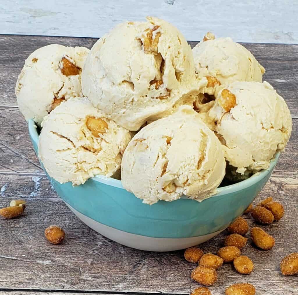 Blue bowl full of scoops of peanut butter ice cream with honey roasted peanuts on wooden surface.