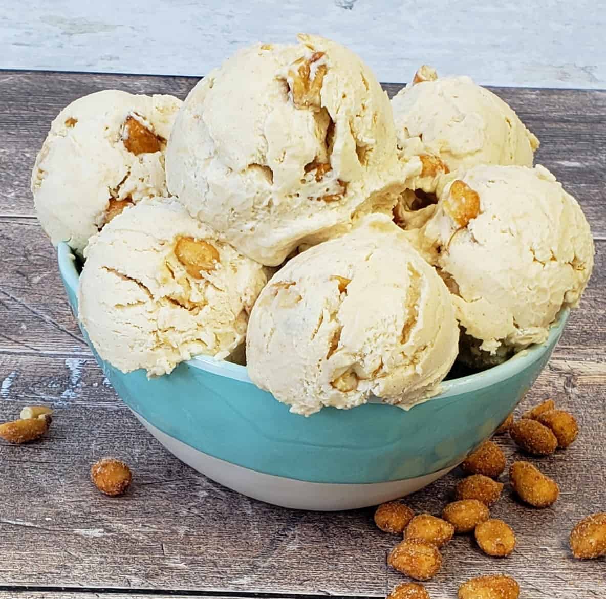 Bowl of scoops of peanut butter ice cream with peanuts on wooden surface.