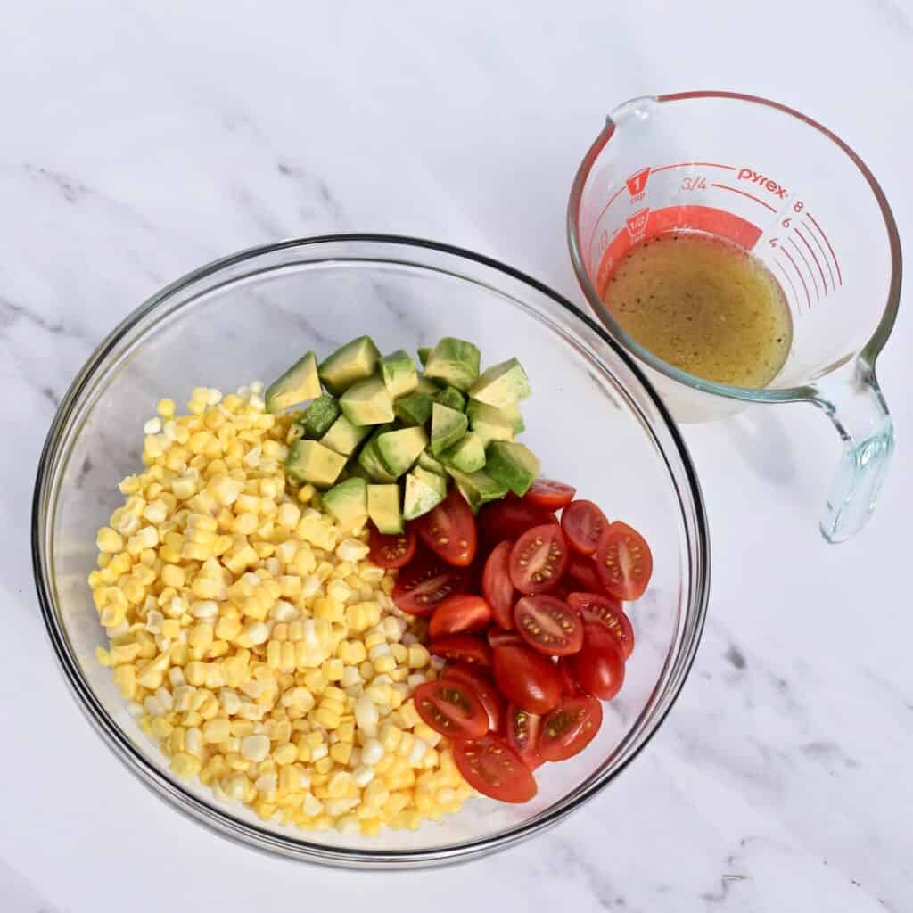 Chopped ingredients for corn salad in a bowl with measuring cup of vinaigrette.